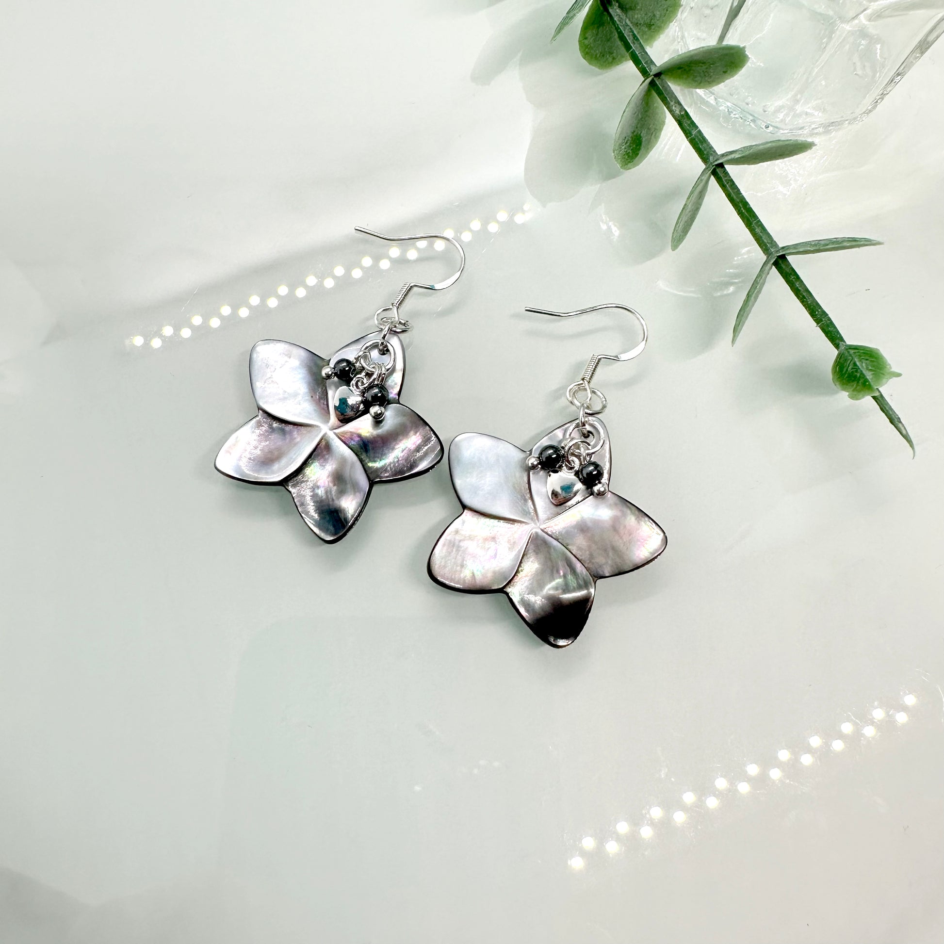 Abalone shell carved flower shapes with iridescent grey shell petals, and with small Hematite balls and silver hearts layered on top, drop earrings with sterling silver components
