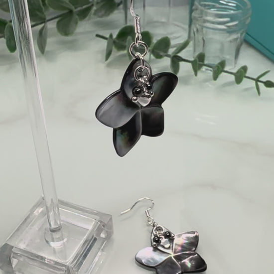 Video showing Abalone shell carved flower shapes with iridescent grey shell petals, and with small Hematite and silver hearts layered on top, drop earrings with sterling silver components