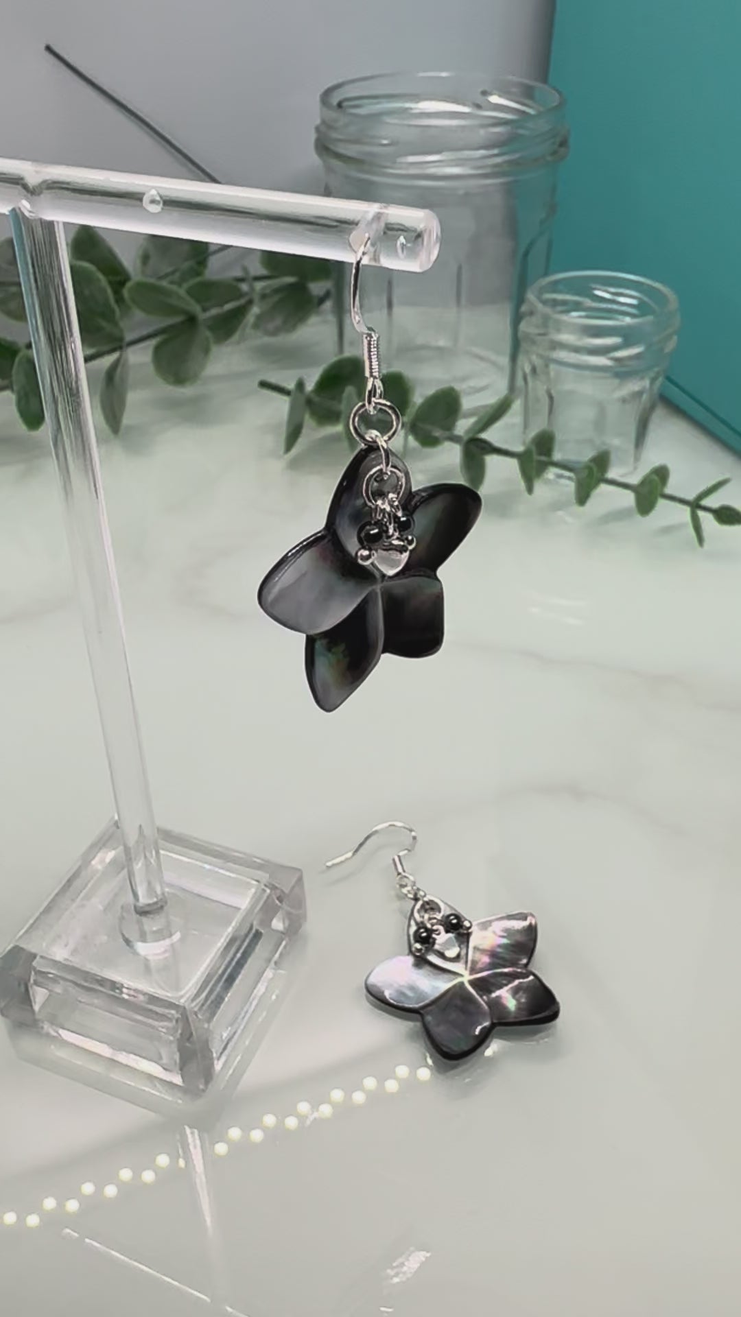 Video showing Abalone shell carved flower shapes with iridescent grey shell petals, and with small Hematite and silver hearts layered on top, drop earrings with sterling silver components
