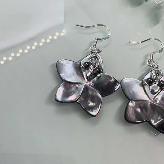 Video showing Abalone shell carved flower shapes with iridescent grey shell petals, and with small Hematite and silver hearts layered on top, drop earrings with sterling silver components